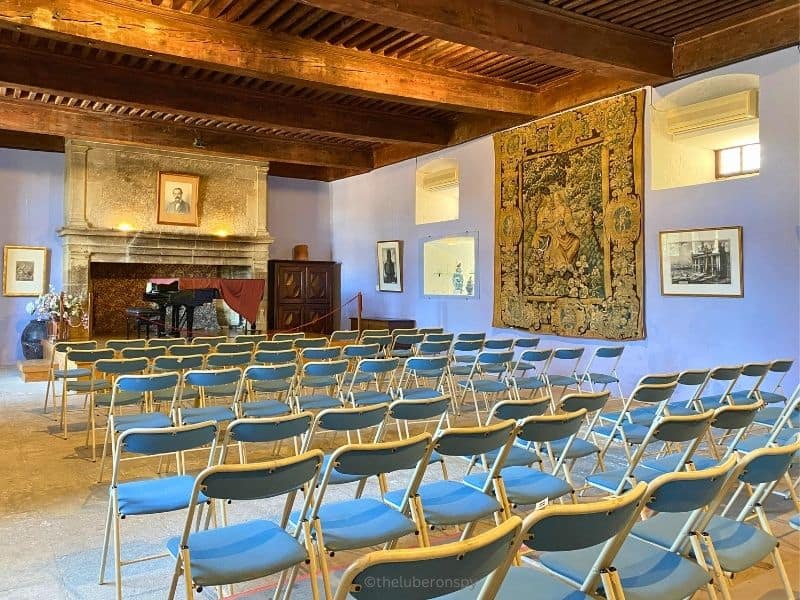 A room in Lourmarin Castle where musical concerts are held. There are chairs and a grand piano.