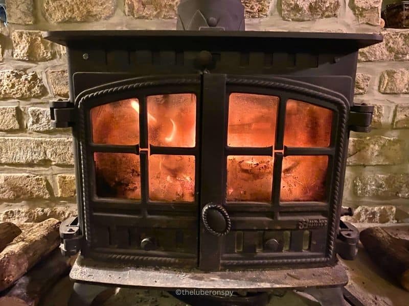 Iron fireplace with fire blazing inside, logs on the side. Good wood is essential to keeping the house warm in Luberon during winter.