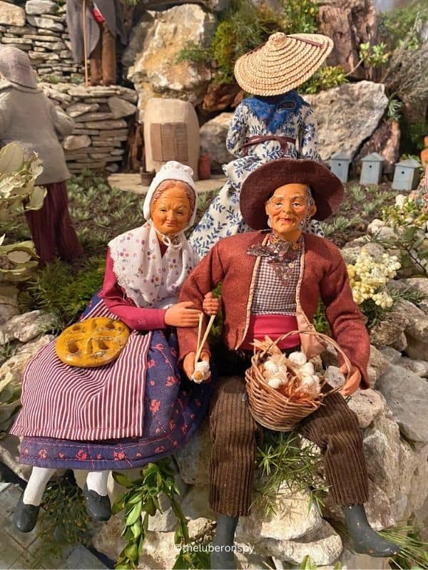 Two Provenรงal santons depicting local professions: The old lady has bread on her lap and the old man has a basket of eggs.