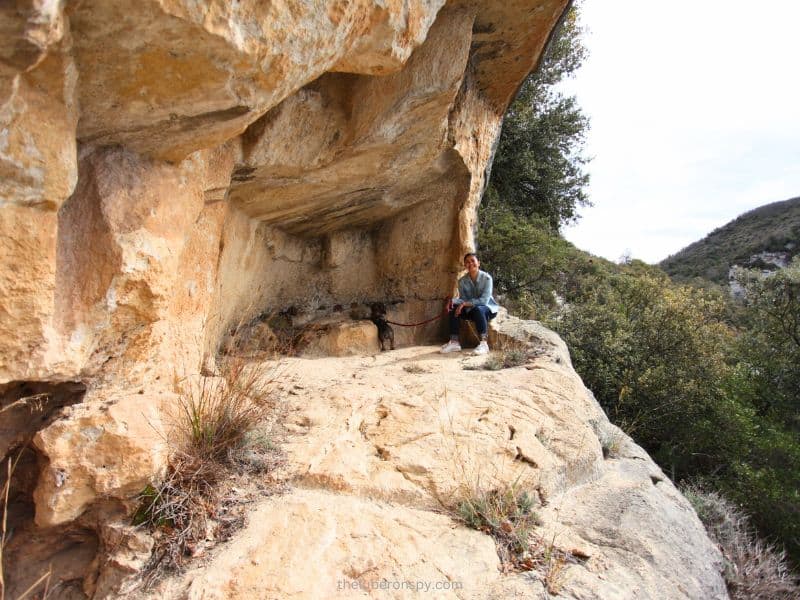 The writer takes a rest in a natural limestone crevice at Buoux, with a leashed dog beside her, surrounded by scrubland vegetation.