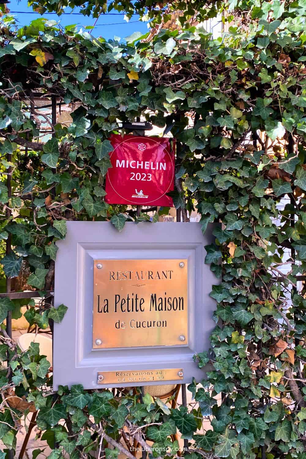 Entrance sign of 'La Petite Maison' a Michelin-starred restaurant in Cucuron, surrounded by lush green ivy.