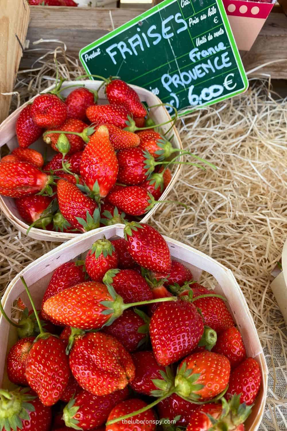 Fresh, bright red strawberries in baskets at a market stall in Luberon, with a sign indicating the price.