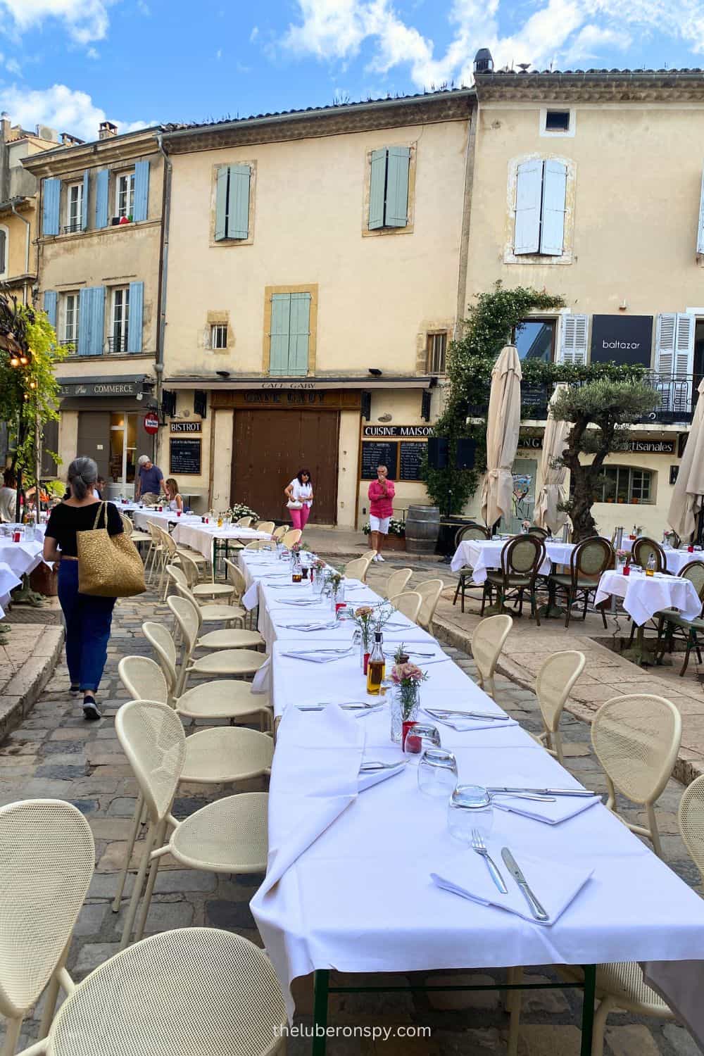 Tables set for an outdoor event in Lourmarin, France, with white tablecloths and rustic cobblestone streets, ready for the Fรชte de la Musique celebration.