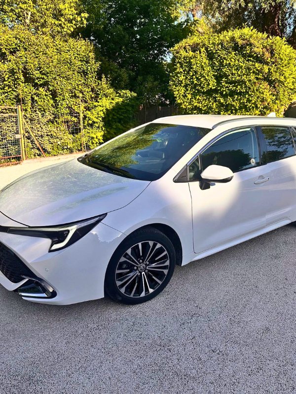 Sleek white sedan parked on a sunny residential driveway in Provence, with modern design details and a backdrop of lush green hedges and trees.