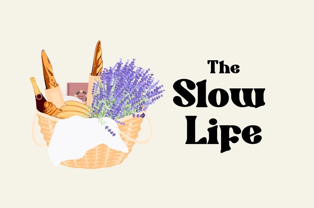 Illustration of a picnic basket filled with baguettes, croissant, a bottle of wine, cheeses, and a bouquet of lavender, beside the text “The Slow Life” on a light background.