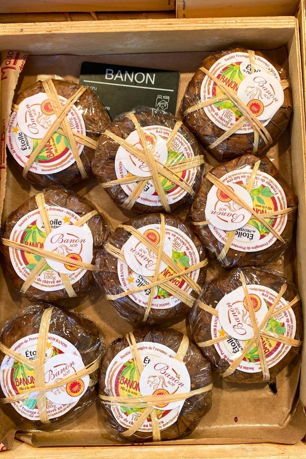Spotted in Lourmarin: Wrapped rounds of Banon goat cheese are stacked in a wooden crate with labels showing Banon AOP, fromage de chรจvre au lait cru.