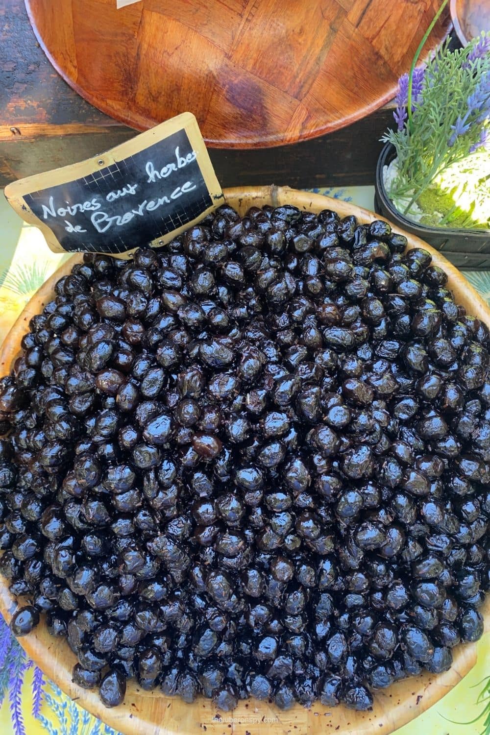 A basket of glossy black olives labeled "Noyaux aux herbes de Provence" at the Lourmarin market.
