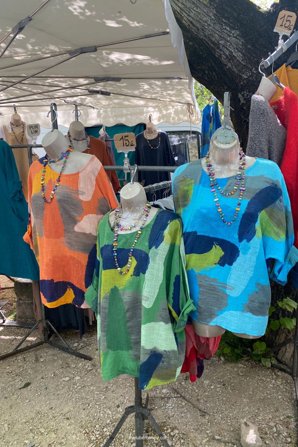 Colorful linen tops and dresses displayed on mannequins at a lively Provence market.