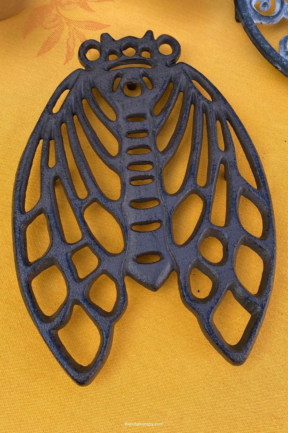 A dark blue cast iron decorative cicada piece is displayed on a golden yellow market tablecloth.