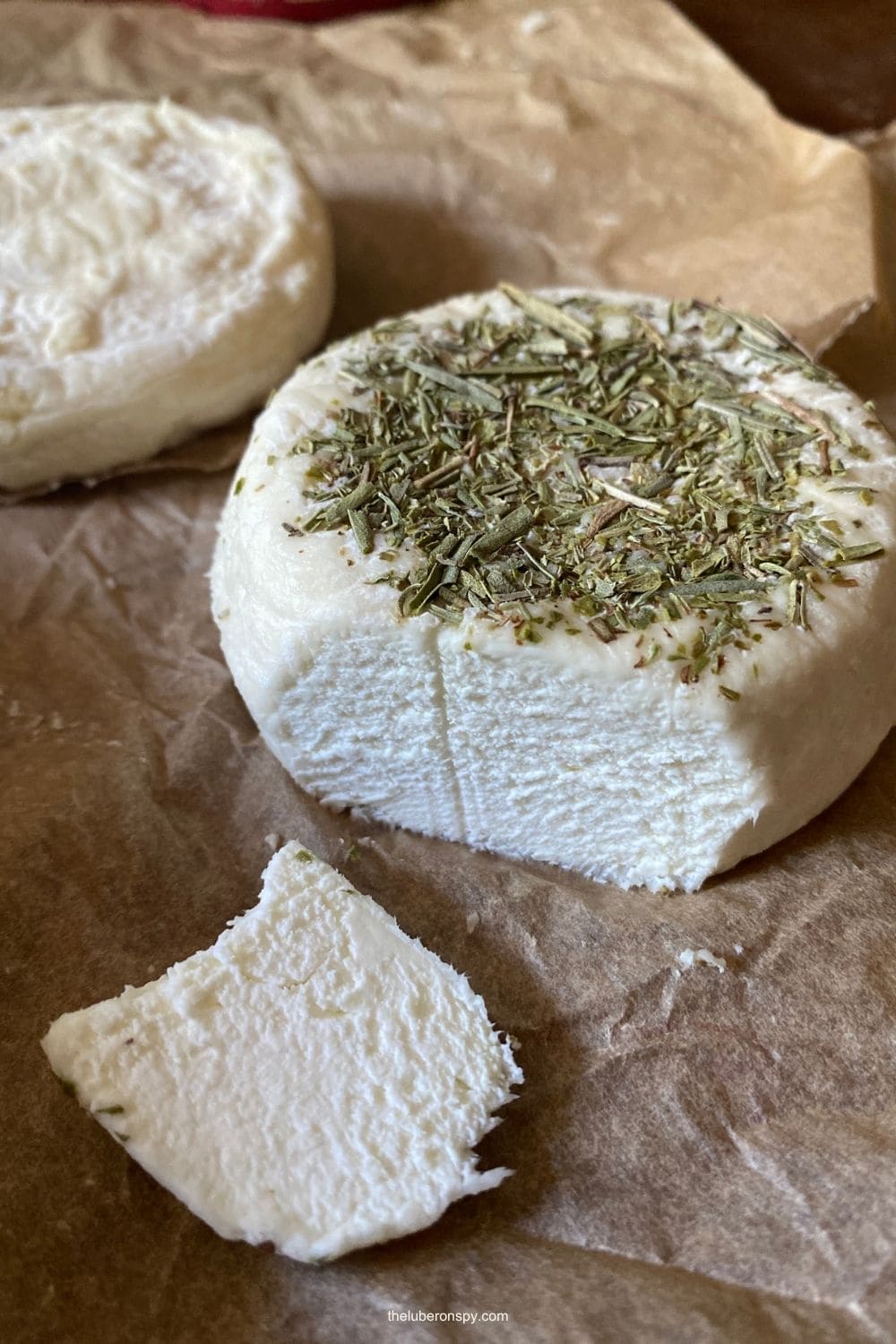 Small rounds of fresh goat cheese, including one topped with dried Provenรงal herbs, are displayed on paper.